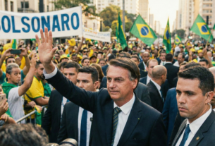 Jair Bolsonaro acenando para a multidão em manifestação com bandeiras do Brasil e cartazes com a palavra 'Bolsonaro' em destaque."
